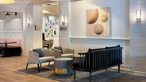 A modern lobby with a seating area featuring a sofa, armchairs, and a coffee table. There is a wall-mounted artwork and a sign indicating the location of the lobby. - Delta Hotels by Marriott Basking Ridge (Basking Ridge)