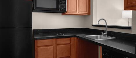 Una cocina con armarios de madera, un microondas negro, un fregadero y un lavavajillas.