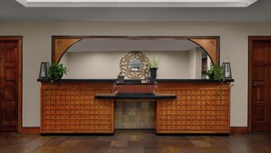 A reception area with a wooden reception desk, a large mirror, and a potted plant.
