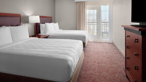 A hotel room with two beds, a TV, a dresser, and a window with curtains.