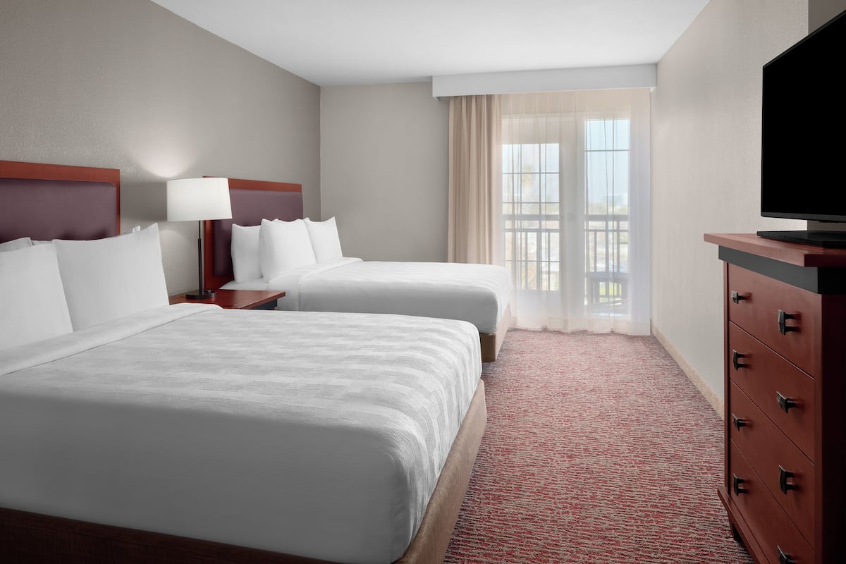 A hotel room with two beds, a TV, a dresser, and a window with curtains.