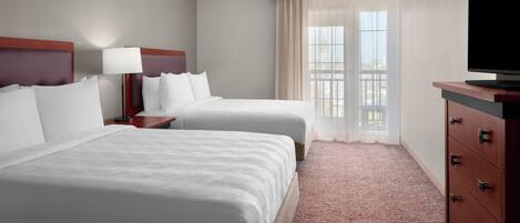 A hotel room with two beds, a TV, a dresser, and a window with curtains.