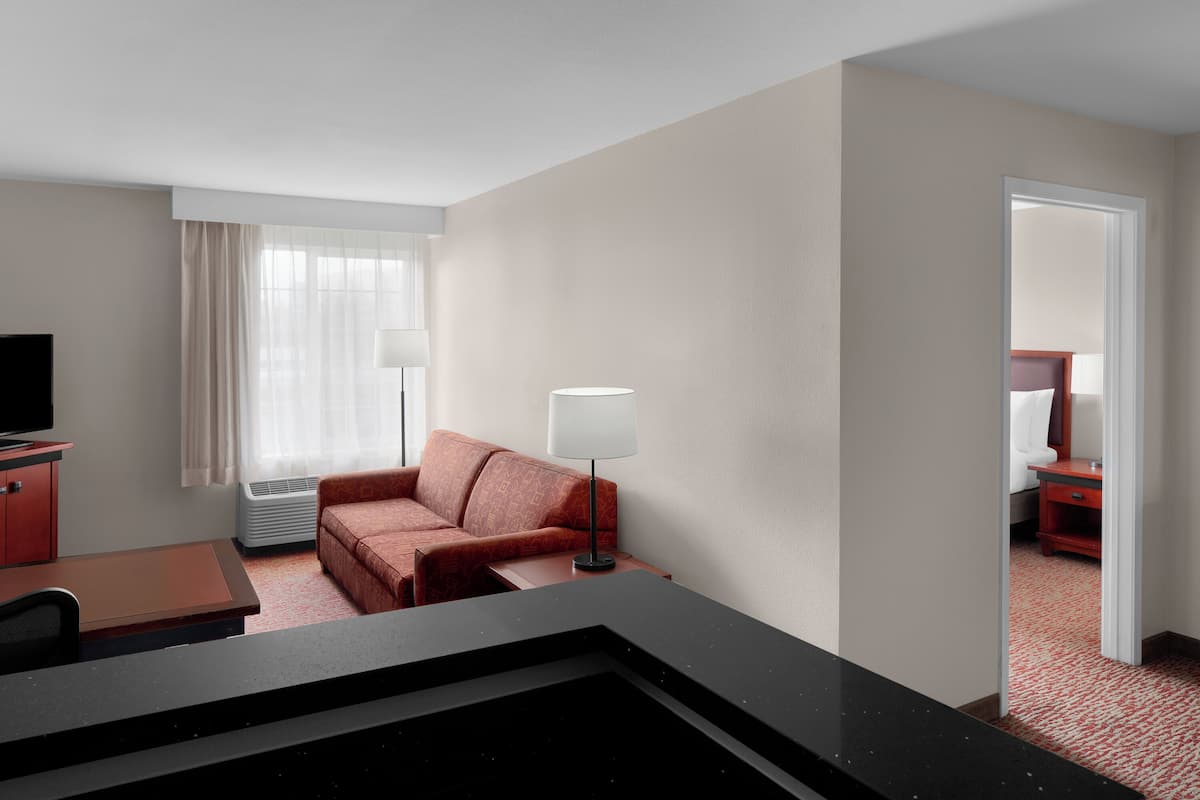 A hotel room with a desk, a red sofa, a lamp, and a television.