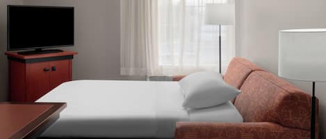 Habitación de hotel con cama, televisión sobre un mueble bajo, escritorio, sofá y lámpara.