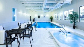 Une piscine intérieure avec un sol carrelé, un escalier d’accès à la piscine et un espace détente avec des chaises et une table.