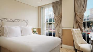 A hotel room with a large bed, a chair, a window with curtains, and a chandelier.