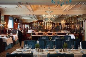 A formal dining room with tables set for service, a waiter in motion, and a chandelier.