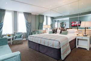 Habitación de hotel con una cama grande, una zona de estar con una silla y una mesa, un espejo y un televisor.
