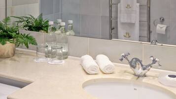 A bathroom with a sink, two rolled towels, a mirror, and a plant.