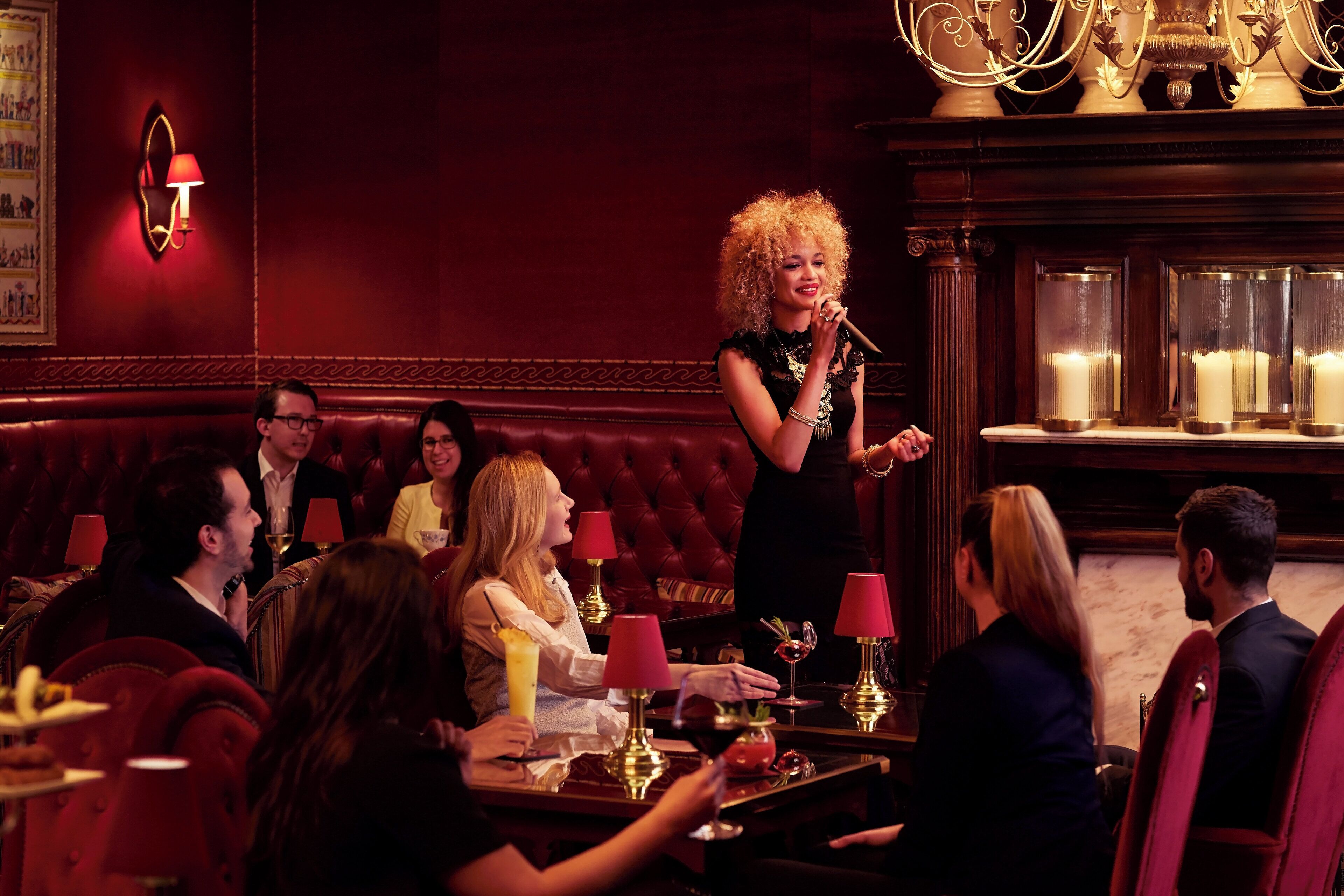 A person speaking at a microphone in a dimly lit room with red walls and a chandelier.