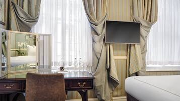 A hotel room with a bed, a desk with a mirror, a chair, and a TV mounted on the wall.