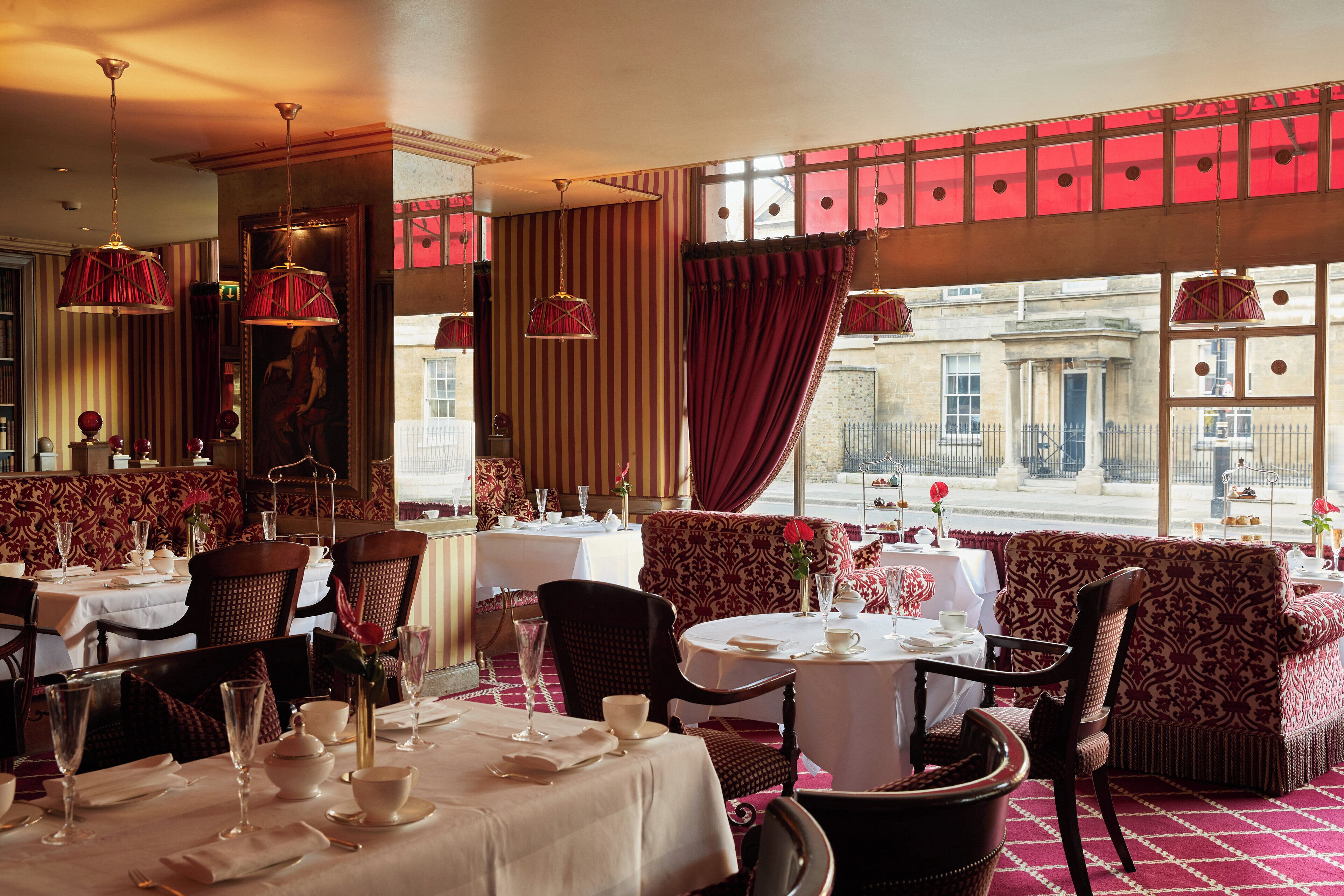 A dining area with tables set for service, chairs, and a view of the street through large windows.