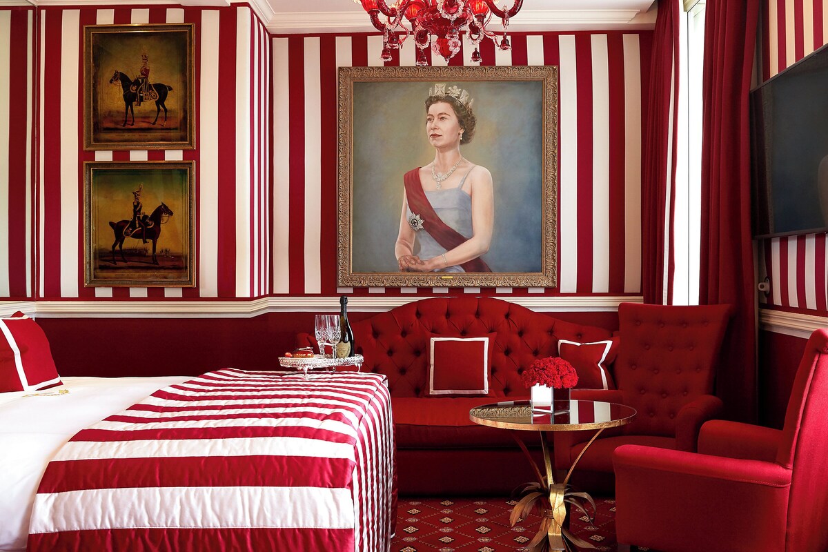Une pièce avec un grand lit, un canapé rouge, une petite table ronde et un grand portrait encadré accroché au mur.
