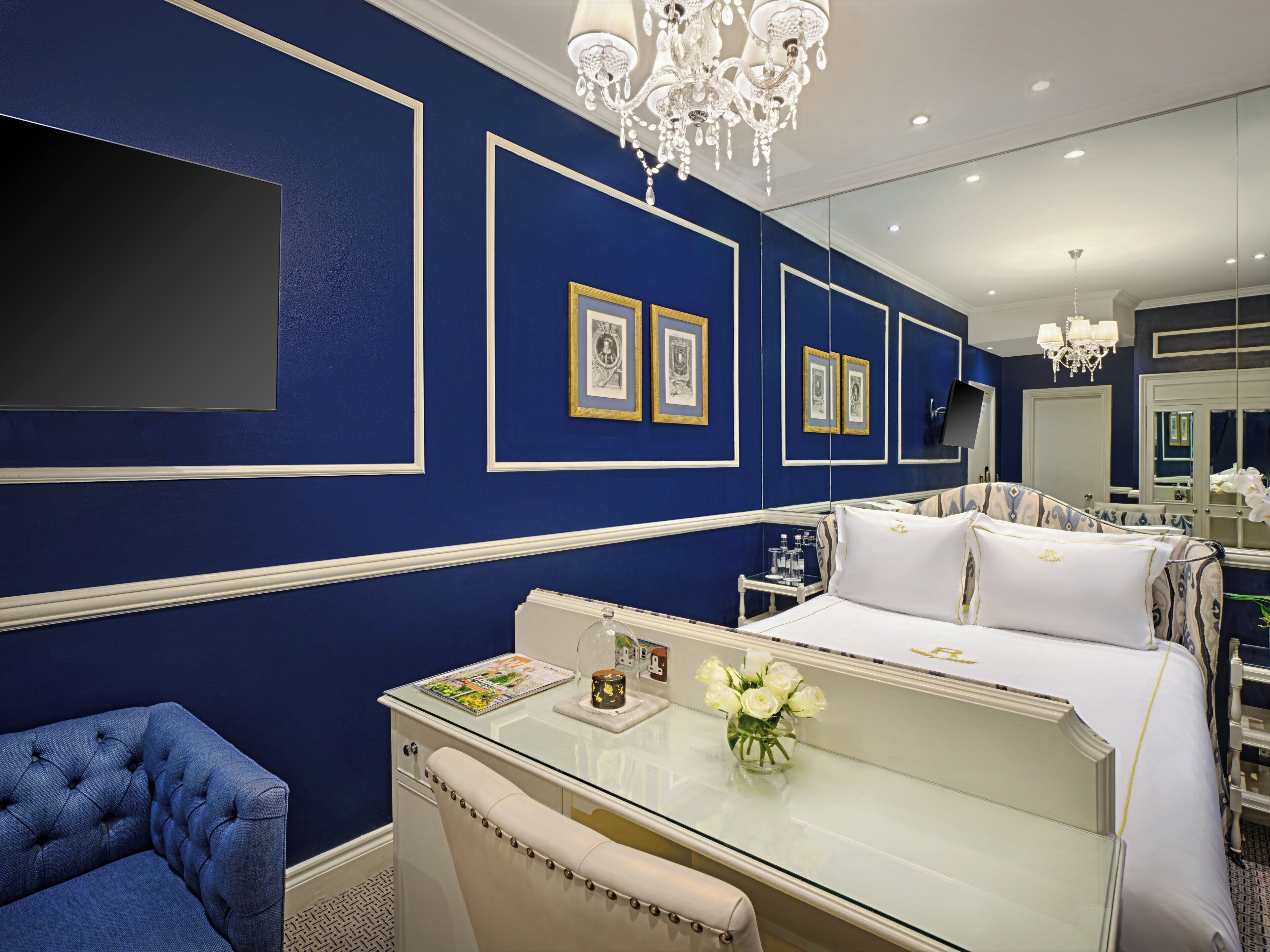 Ein luxuriöses Hotelzimmer mit einem großen Bett, einem Glastisch, einem blauen Sessel und einer Kristallleuchter.