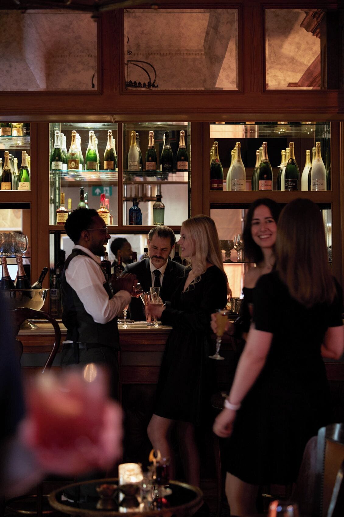 Un bar avec des étagères remplies de bouteilles et de verres, un barman et des clients.
