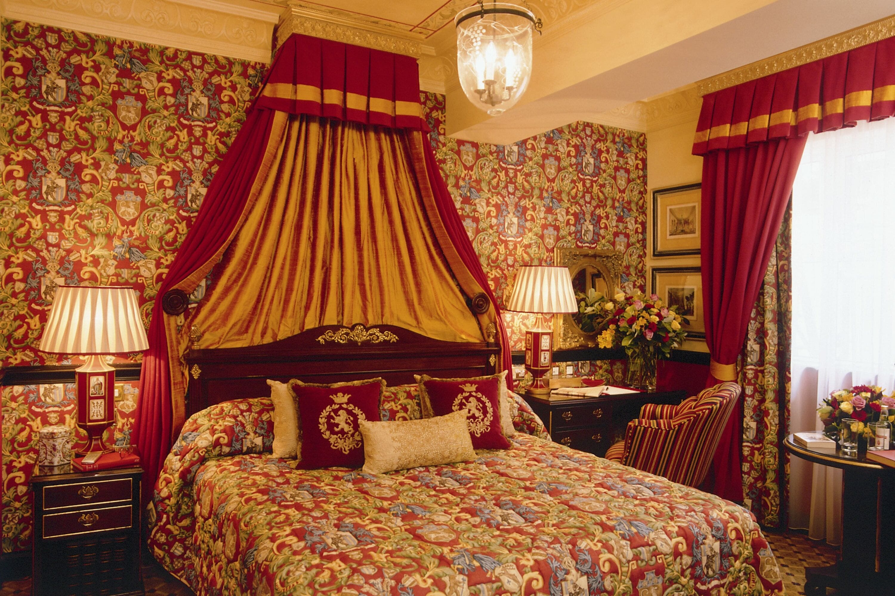 A luxurious bedroom with a four-poster bed, ornate curtains, and floral wallpaper.