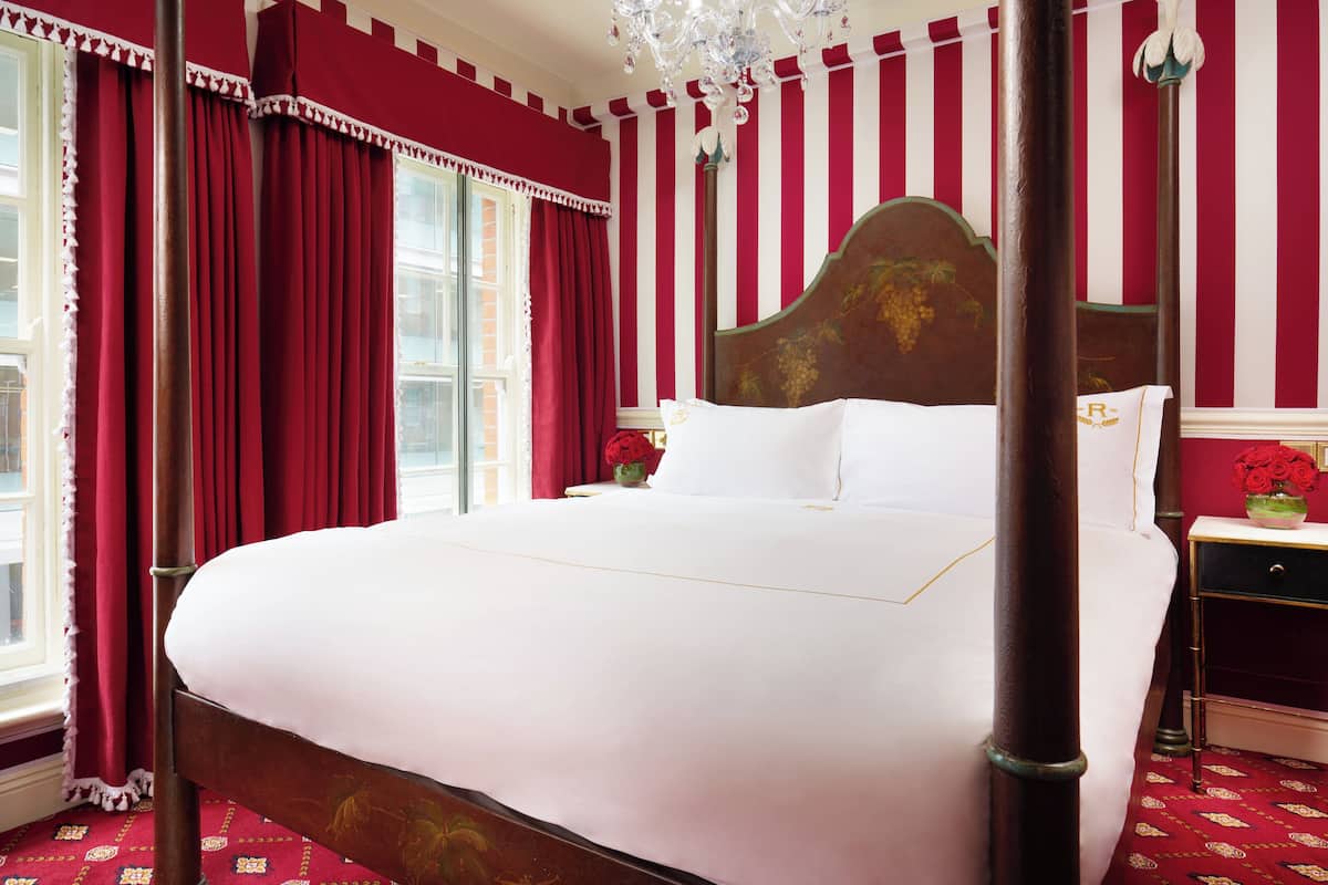 A four-poster bed with white linens, red curtains, and a chandelier.