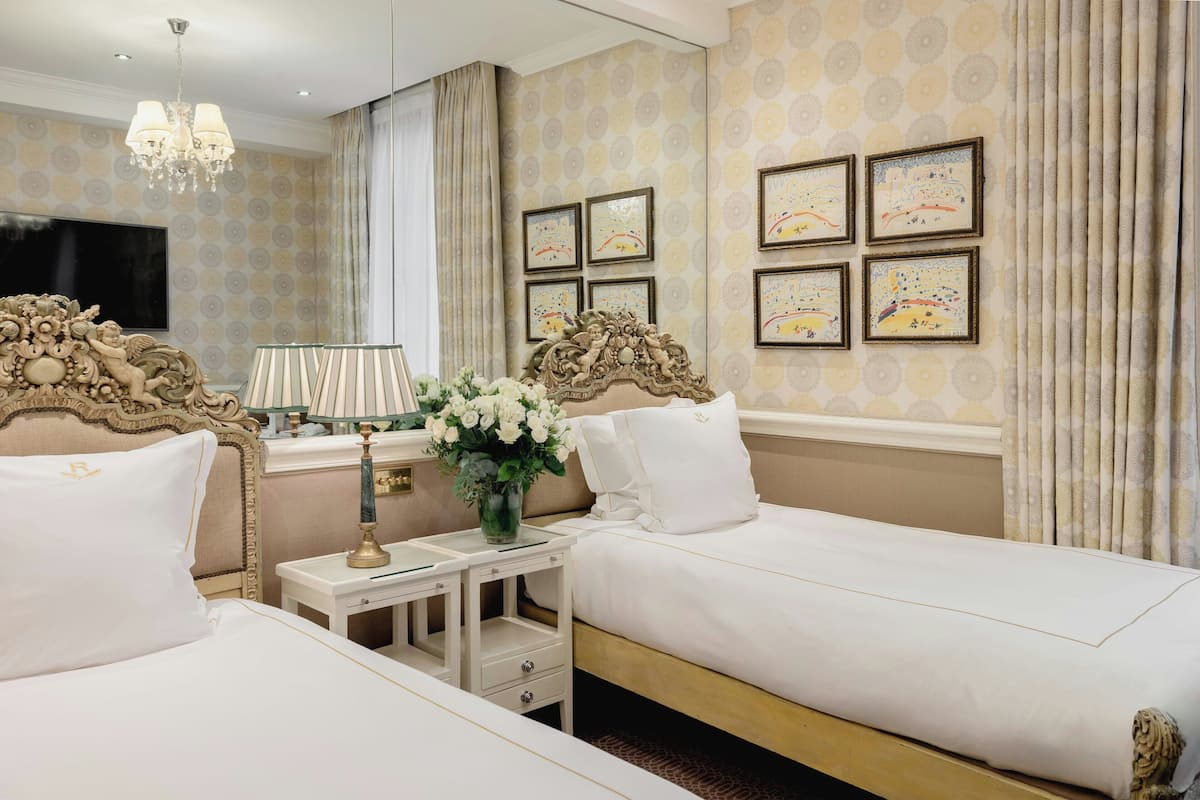 A hotel room with two beds, a chandelier, a TV, and artwork on the walls.