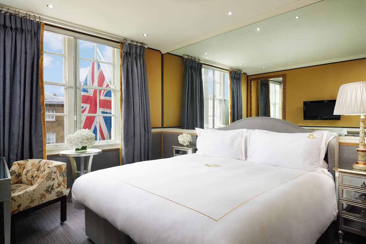 A hotel room with a large bed, a small table with a vase of flowers, a chair, and a window with curtains.