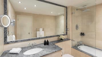 Un baño moderno con encimera de granito, dos lavamanos, un espejo grande y una cabina de ducha con mampara de vidrio.