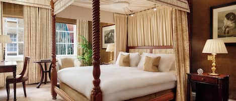 A four-poster bed with a canopy, a desk with a chair, a small table, and a lamp.