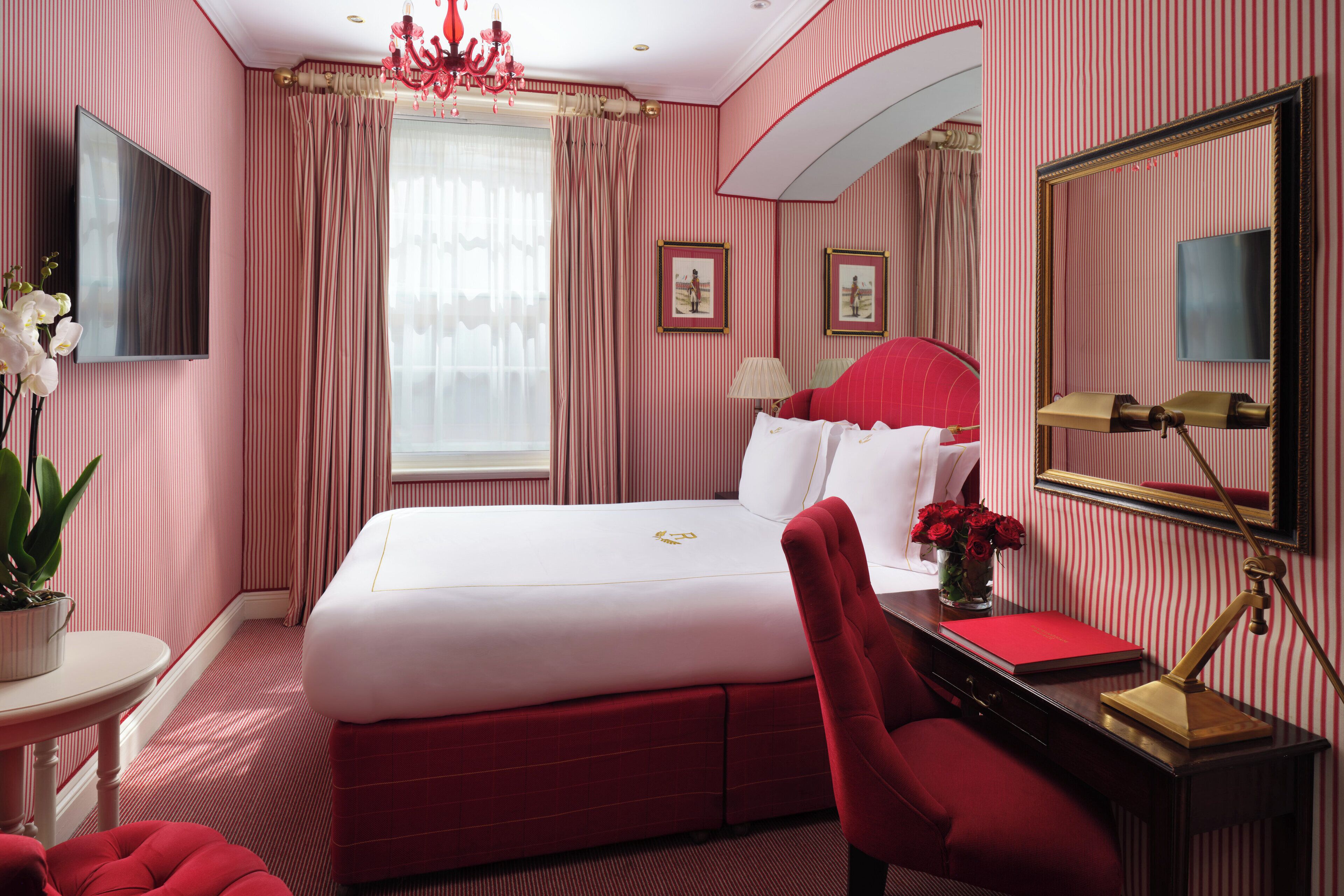 A hotel room with a large bed, a desk with a lamp, a chair, a TV, and a window with curtains.