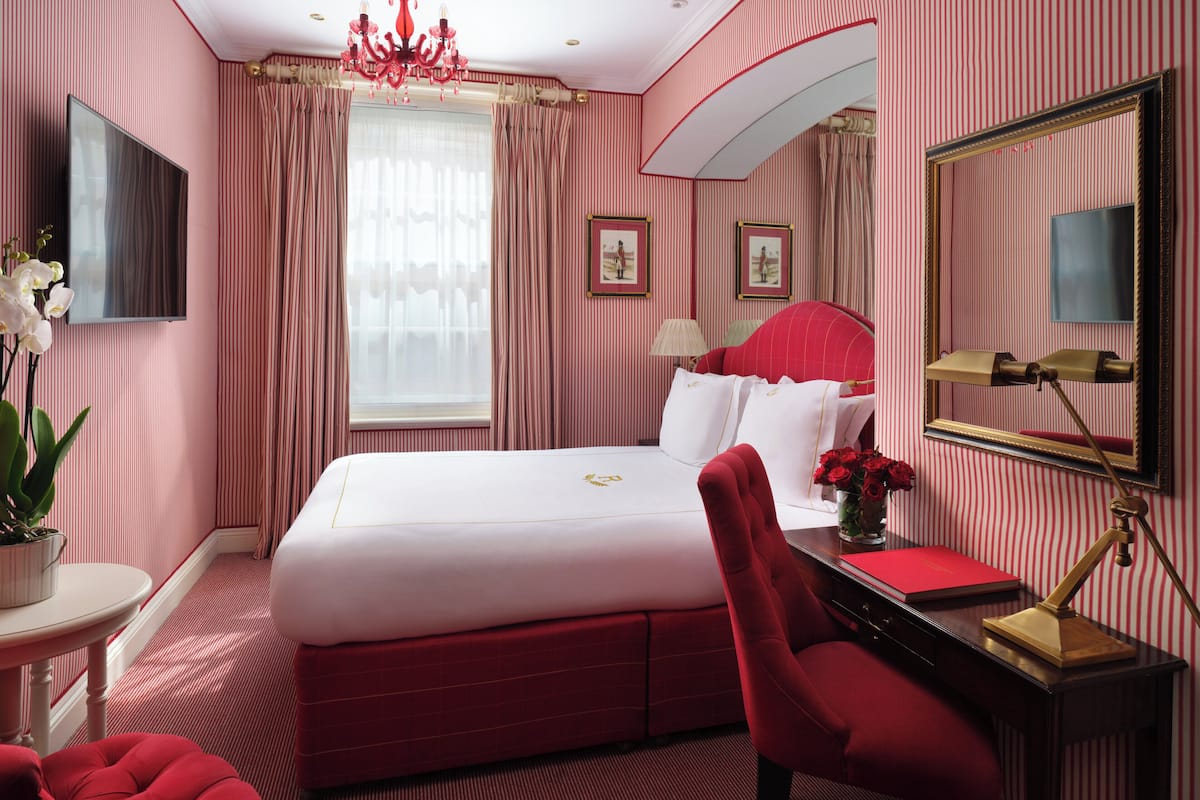 A hotel room with a large bed, a desk with a lamp, a chair, a TV, and a window with curtains.