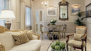 Una sala de estar con un sofá, sillones, una mesa de centro con alcachofas, una mesa de comedor con sillas, una araña y un espejo grande.