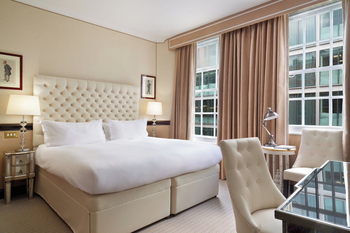 Une chambre d’hôtel avec un grand lit, deux tables de chevet avec des lampes, une chaise et une petite table.