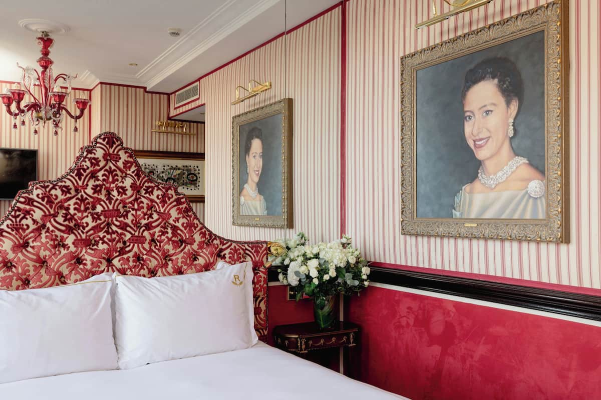 A hotel room with a large, ornate bed, a chandelier, and two framed portraits on the wall.