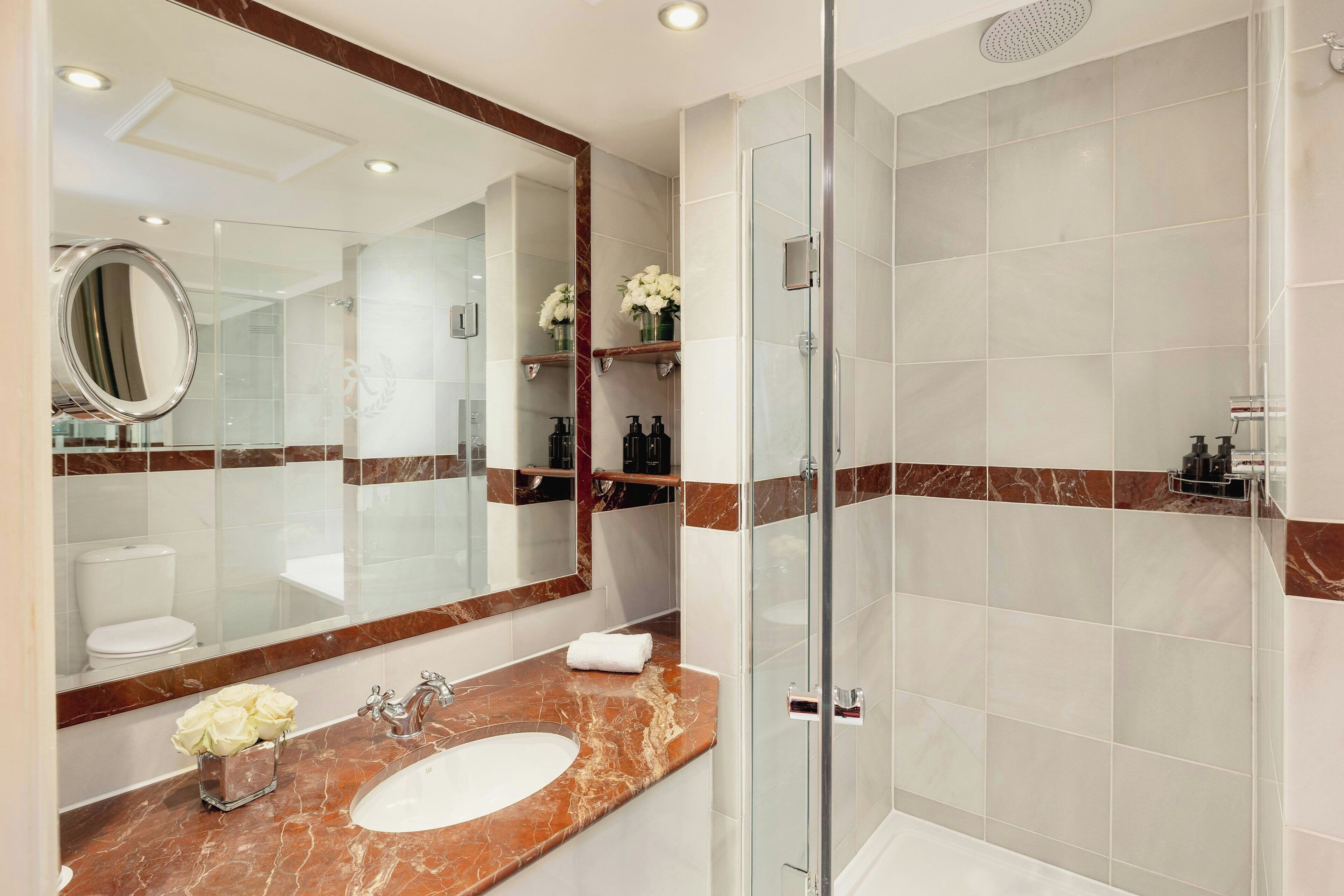 A modern bathroom with a glass shower enclosure, a marble vanity, and a large mirror.