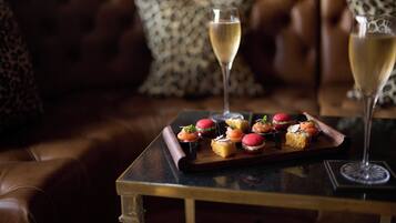A tray of appetizers on a table with two glasses of champagne, set on a leather couch with patterned cushions.