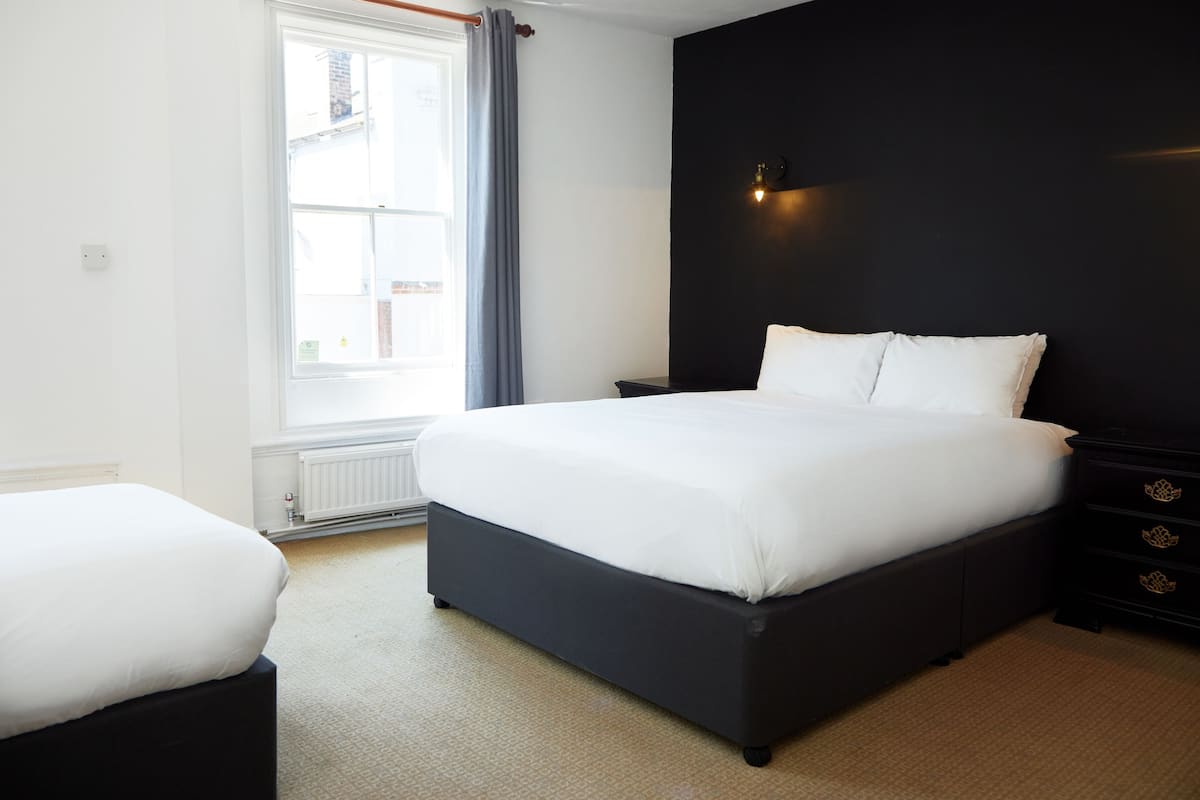A bedroom with a large bed, a bedside table, a dresser, and a window with curtains.