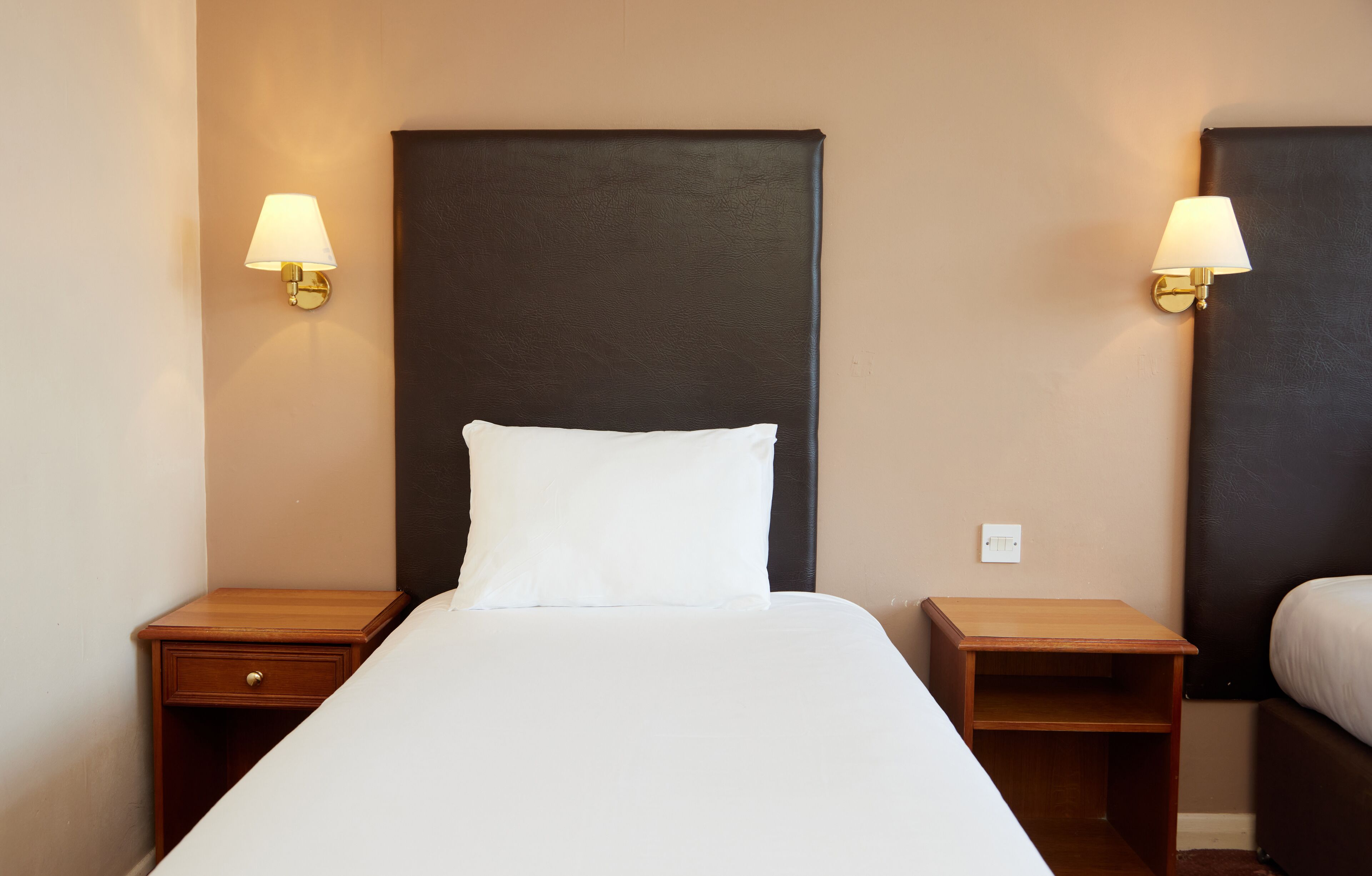 A hotel room with a large bed, two nightstands, and wall-mounted lamps.