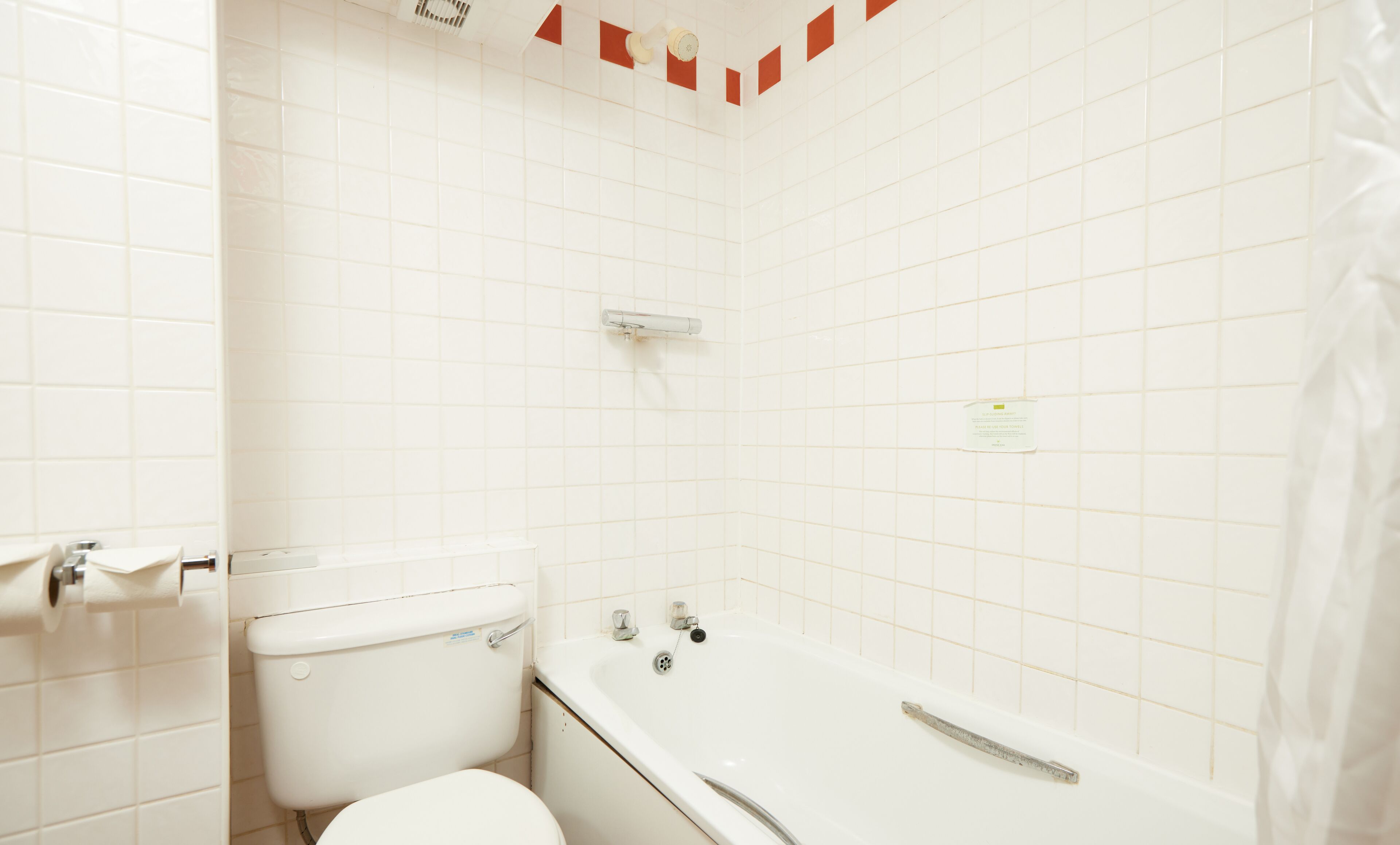 Ein Badezimmer mit weißen Fliesen, einer Toilette, einer Badewanne und einer Duschvorhang.