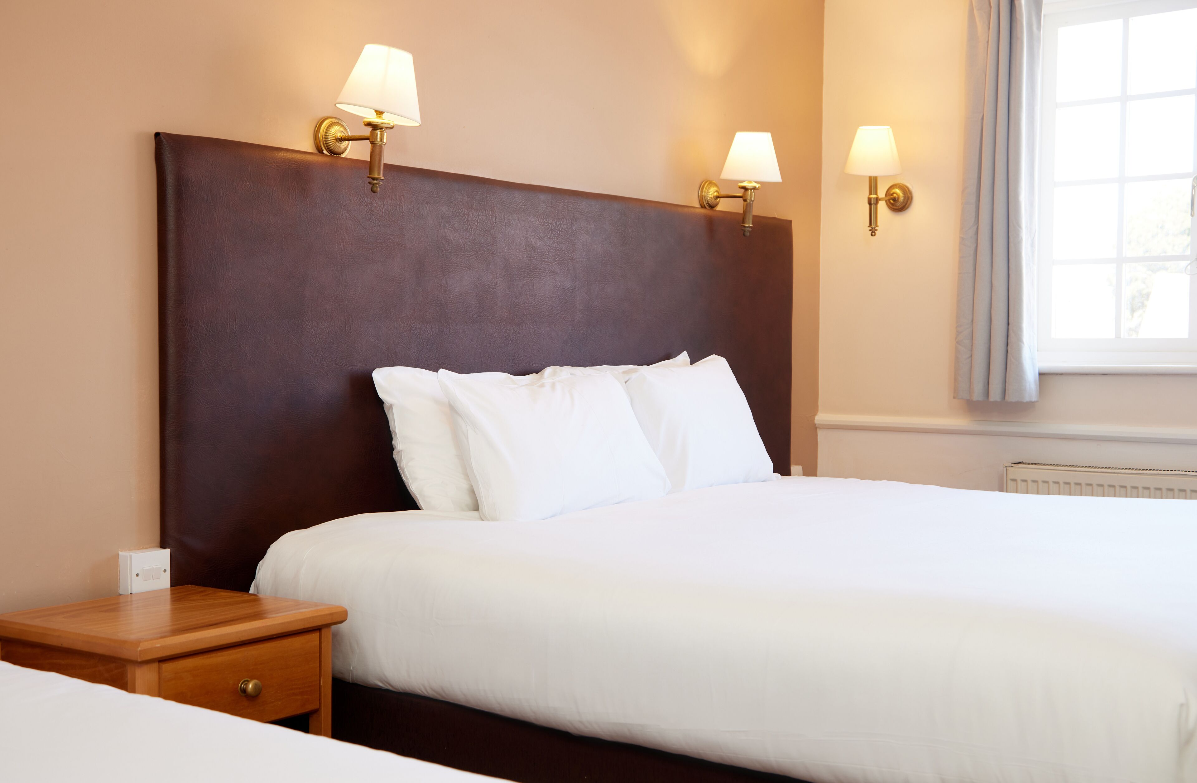 A hotel room with a large bed, two wall-mounted lamps, a nightstand, and a window with curtains.