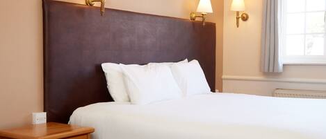 A hotel room with a large bed, two wall-mounted lamps, a nightstand, and a window with curtains.
