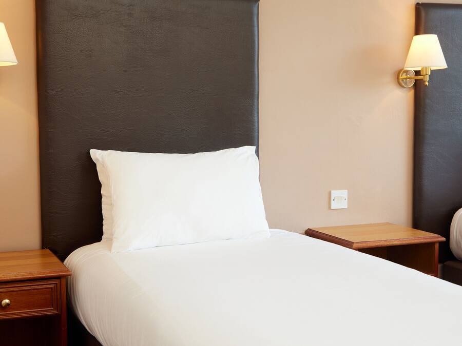 A hotel room with a large bed, two bedside tables, and two wall-mounted lamps.