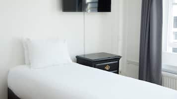 A hotel room with a bed, a nightstand, a flat-screen TV mounted on the wall, and a window with curtains.