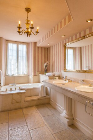 Une salle de bain avec deux lavabos, une baignoire, un lustre, un papier peint à rayures et un grand miroir.