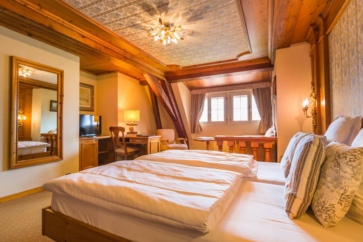 Ein Schlafzimmer mit einem großen Bett, einem Schreibtisch, einem Stuhl, einem Fernseher und einem Spiegel.