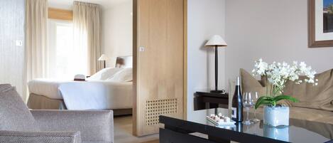 A hotel room with a bed, a sitting area with a sofa and armchair, a coffee table with a vase of flowers, and a lamp.