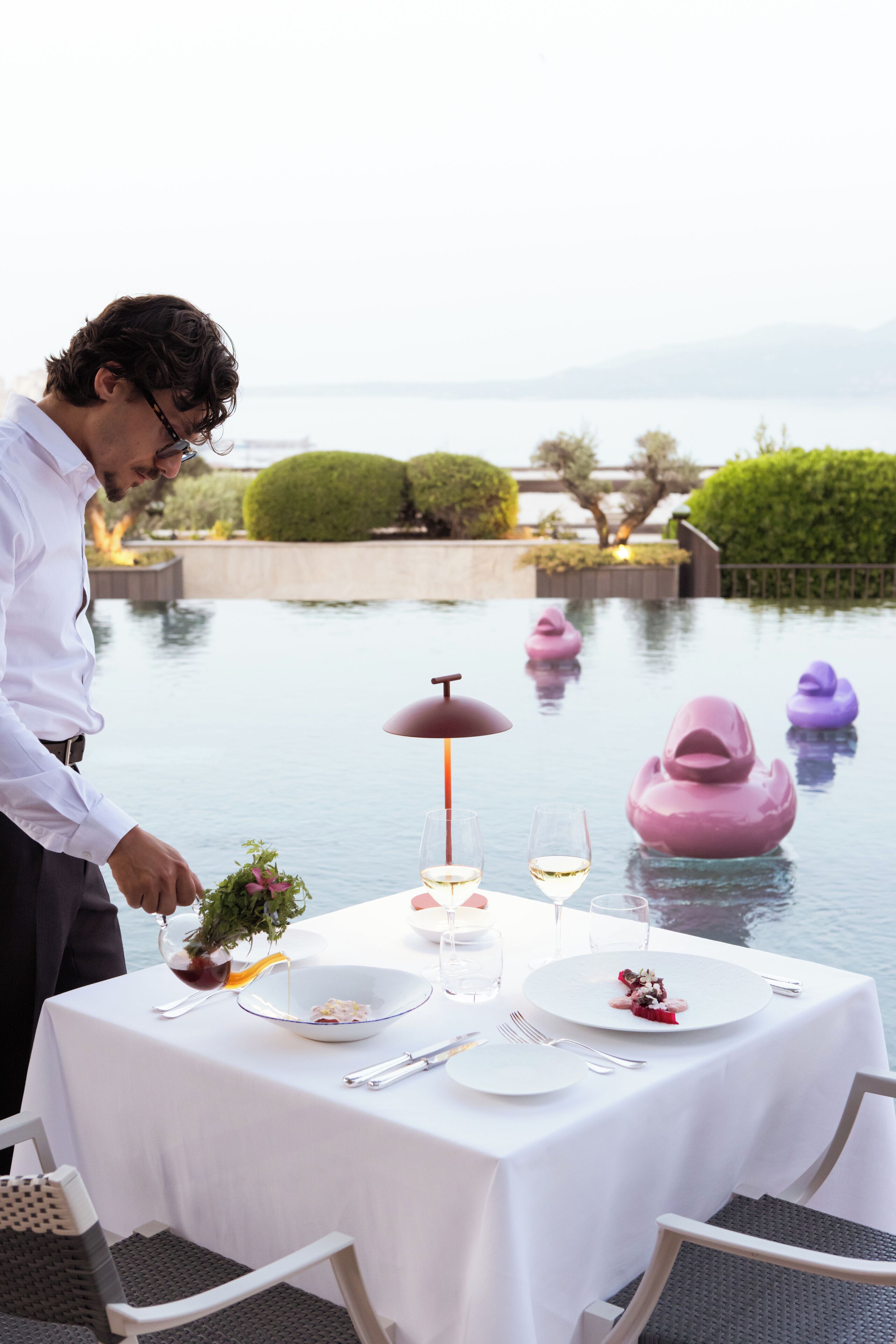 A table set for dining with a view of a body of water and decorative elements.
