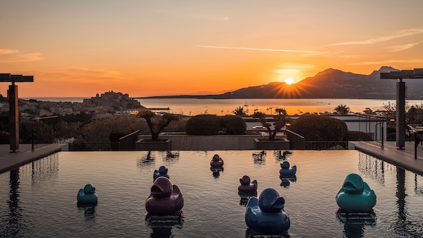 An infinity pool with decorative sculptures, a sunset view, and a cityscape in the background. - La Villa Calvi (Calvi)
