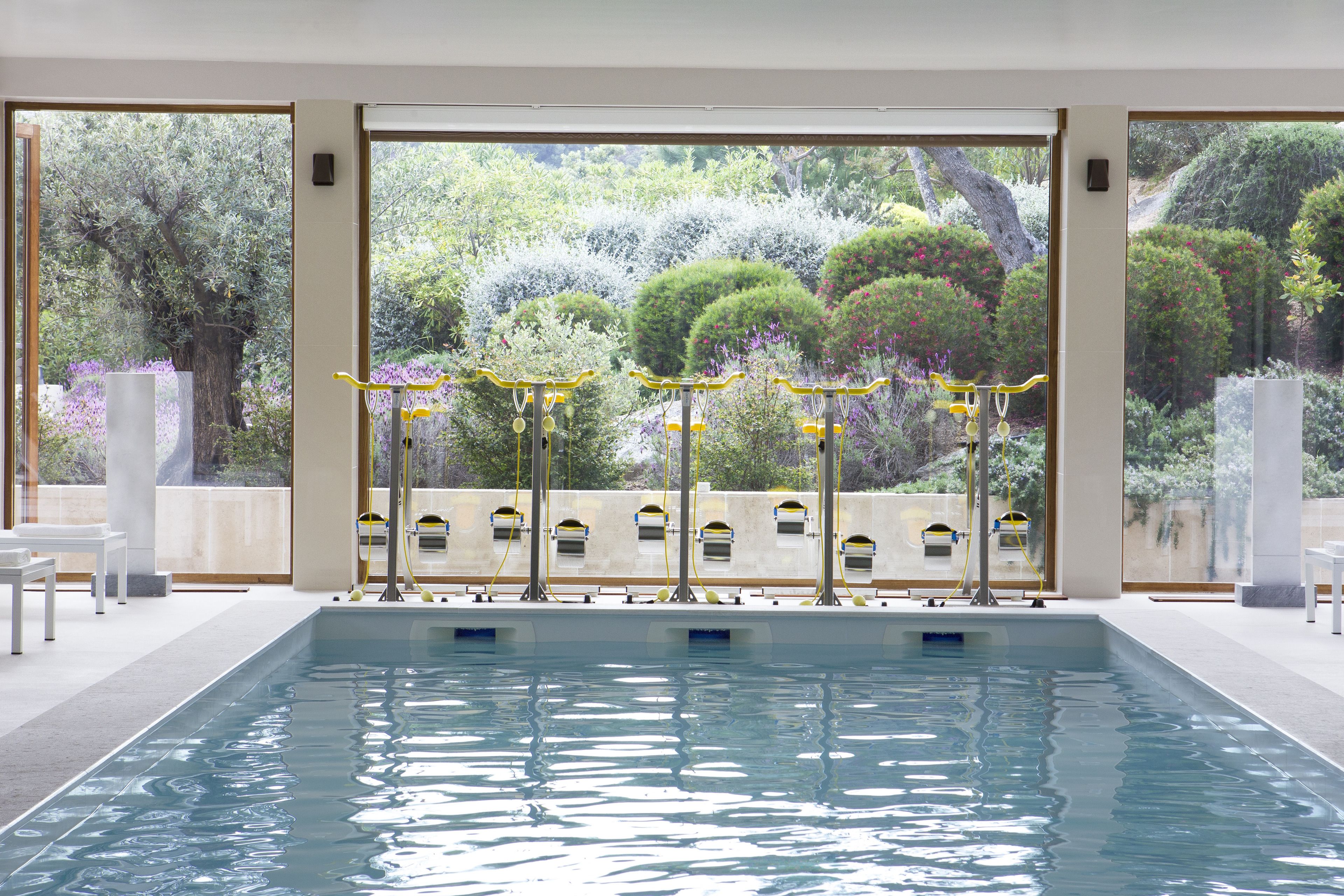 A swimming pool with a view of a garden through large windows.