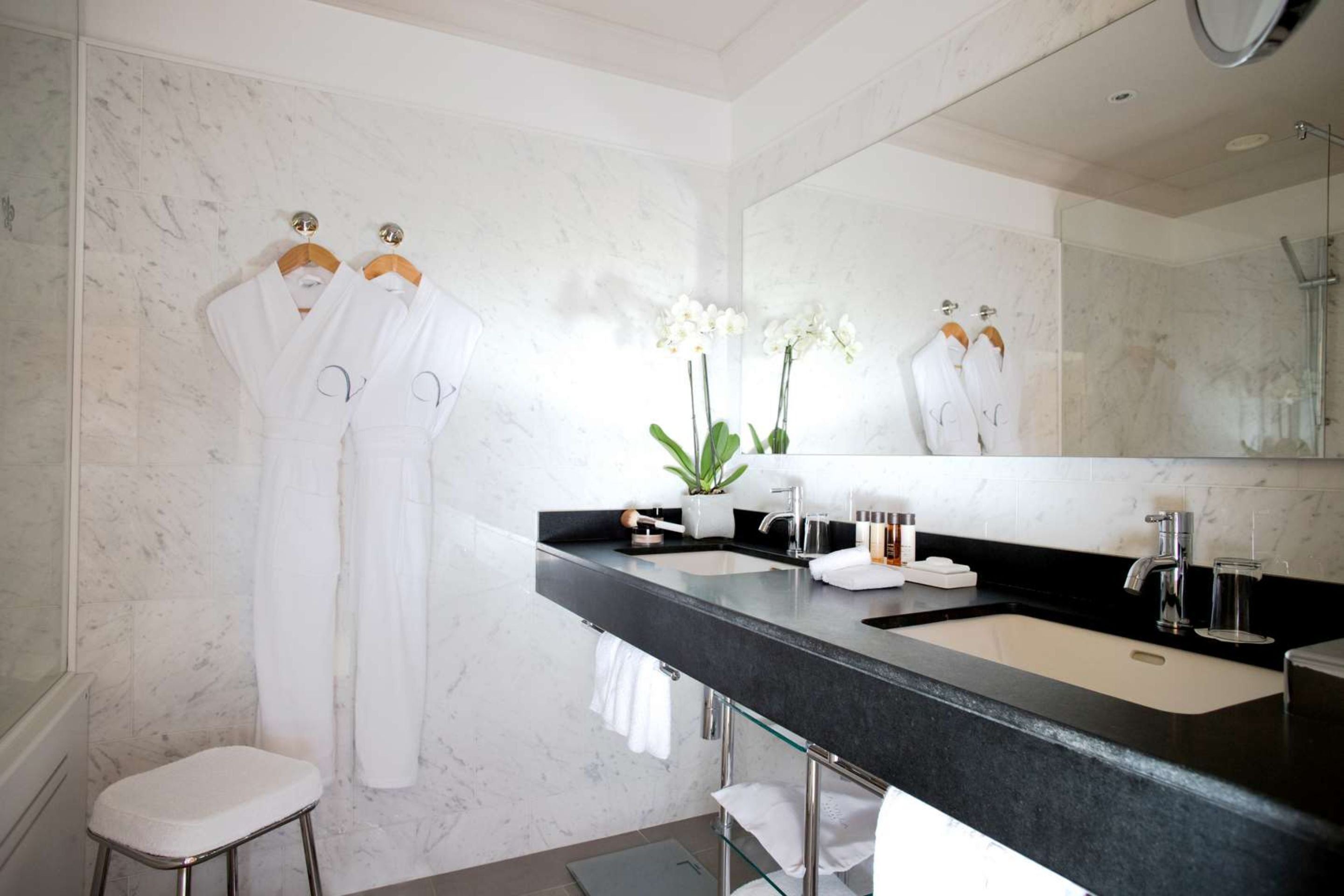A modern bathroom with a marble wall, a black sink, and two white robes hanging on hooks.