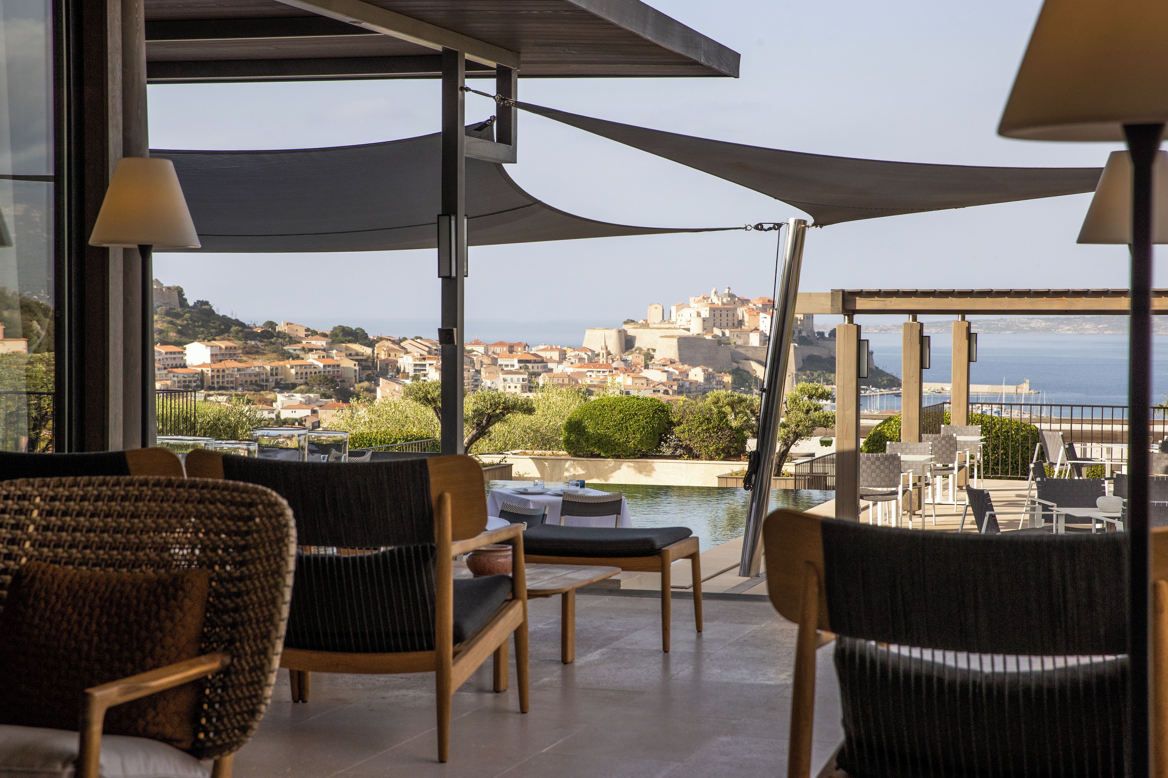 Une terrasse avec des chaises en osier, une table et une vue sur une ville côtière.