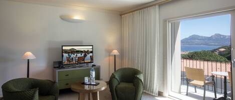 Ein Hotelzimmer mit Balkon, Fernseher, Schreibtisch, zwei Stühlen und einem Bett.