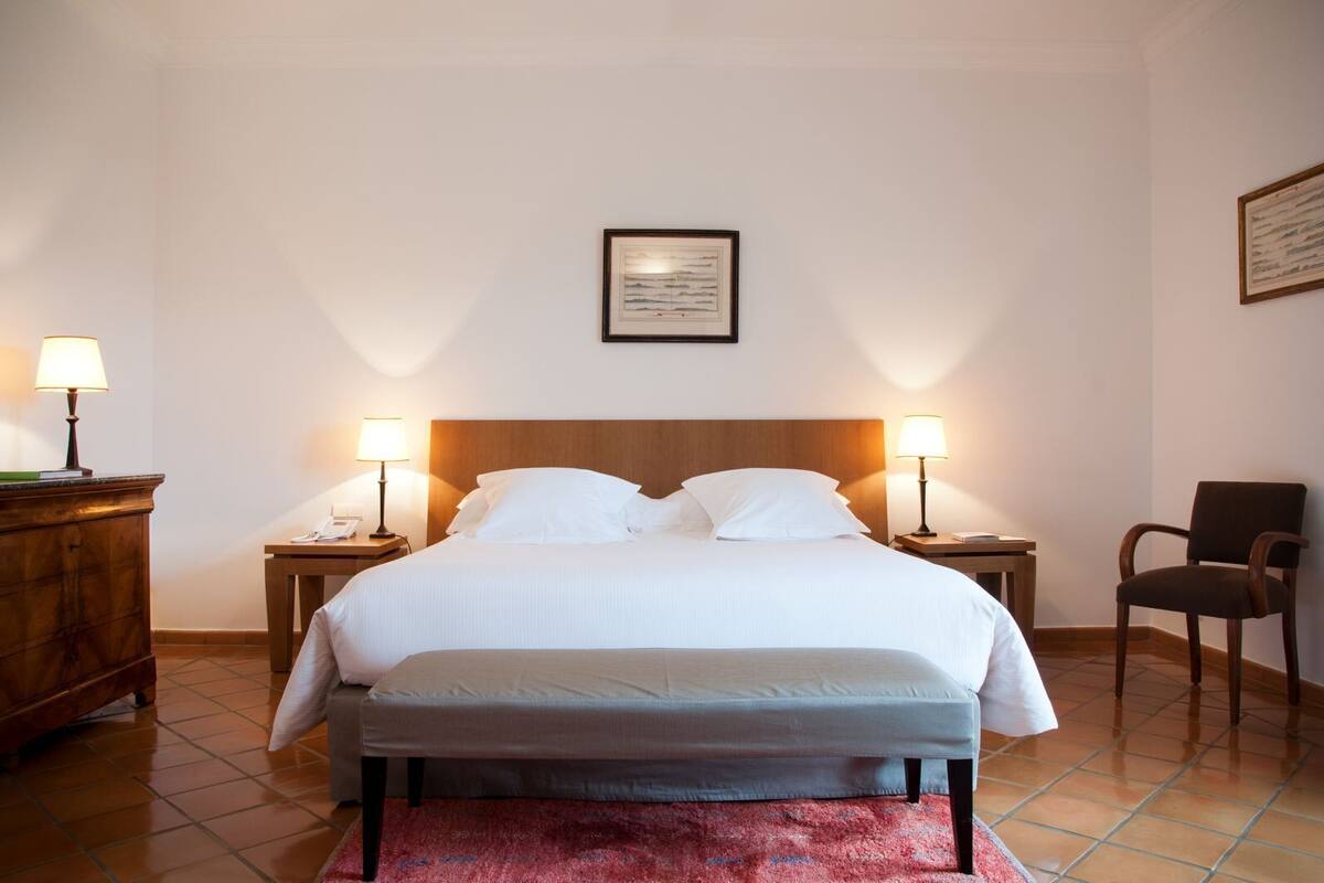 A neatly arranged hotel room with a large bed, two bedside tables with lamps, a chair, and a framed picture on the wall.