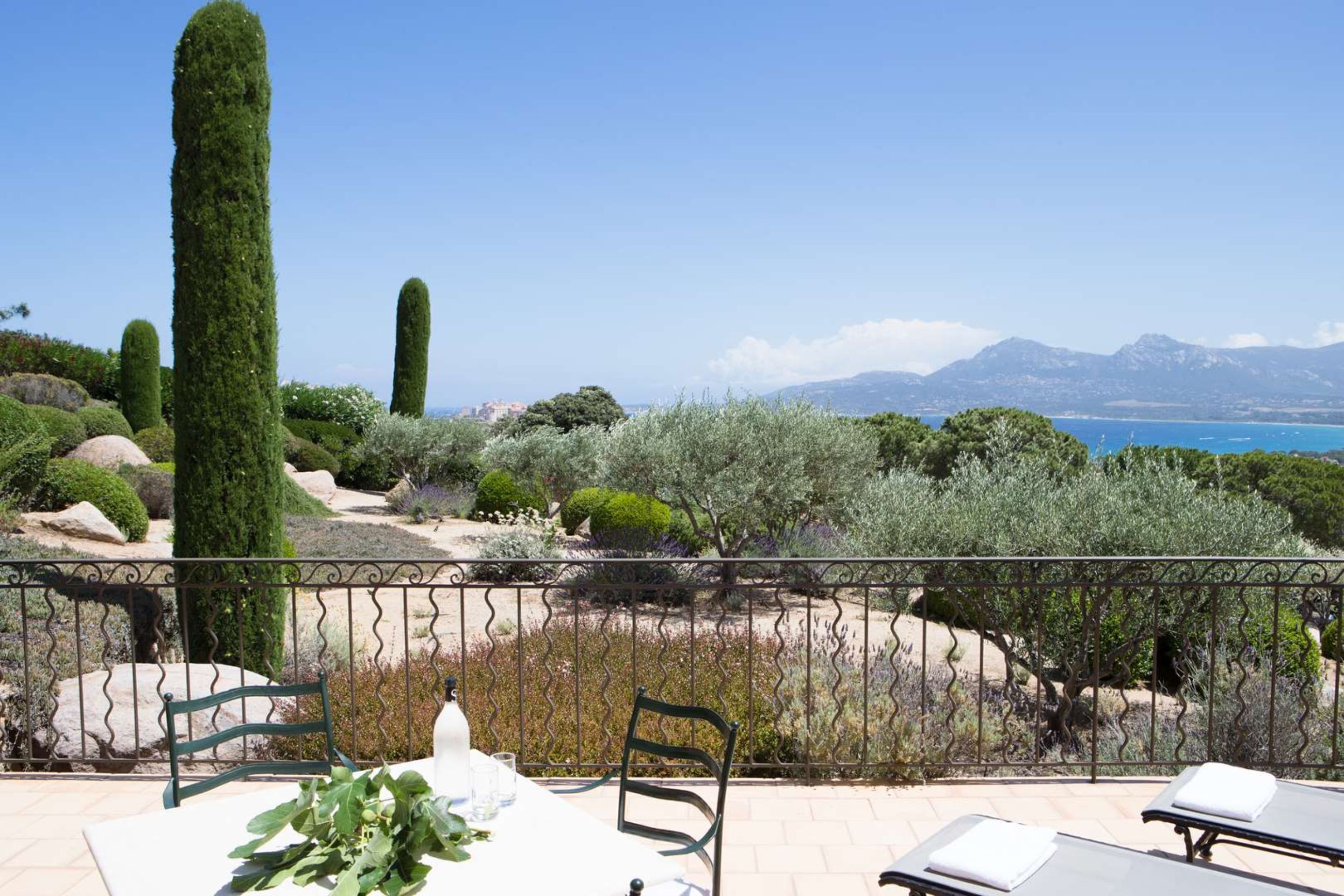 Una terraza con mesa, sillas y vistas al mar y a las montañas.